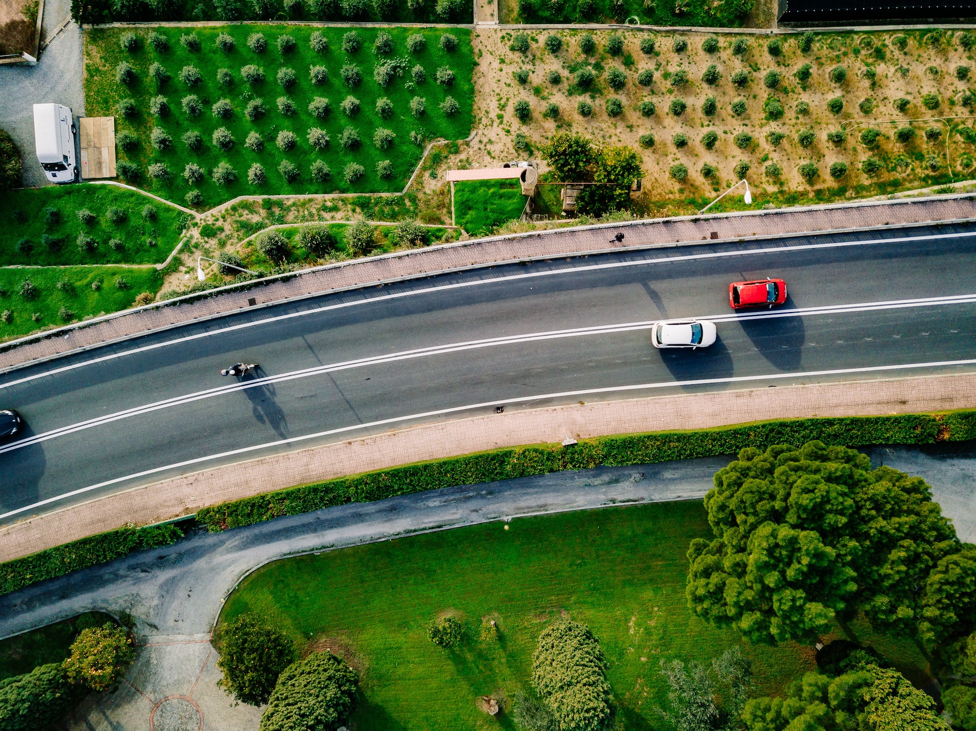 Aerial view of the asphalt road with cars going among the agricultural fields in Italy